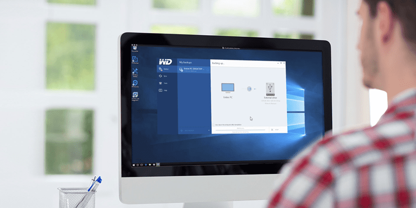 A male in front of an All-in –One desktop, with screen showing some WD utility software